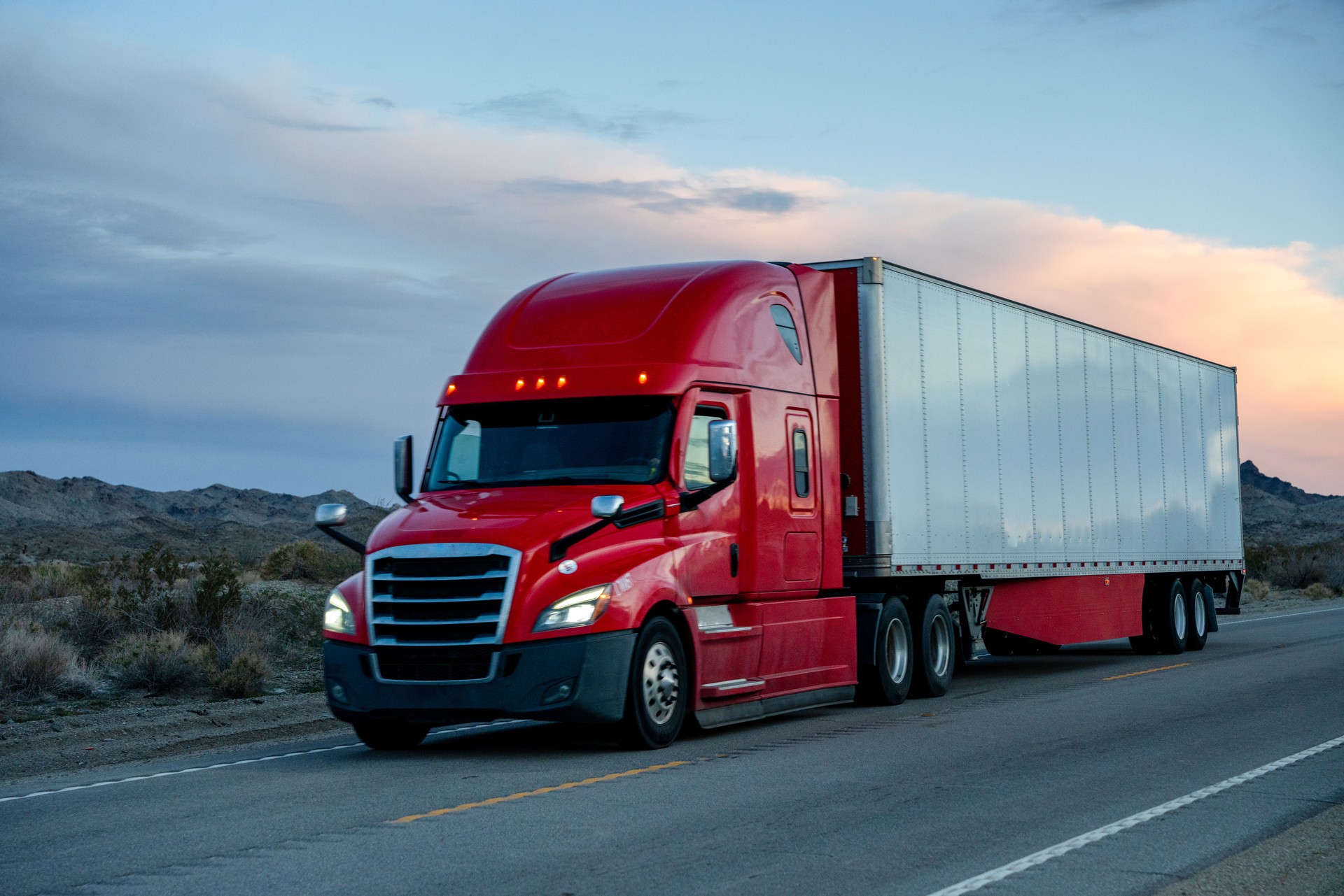 A Red Semi-Truck on a Two-Lane Highway with Beautiful Clouds in the Sky