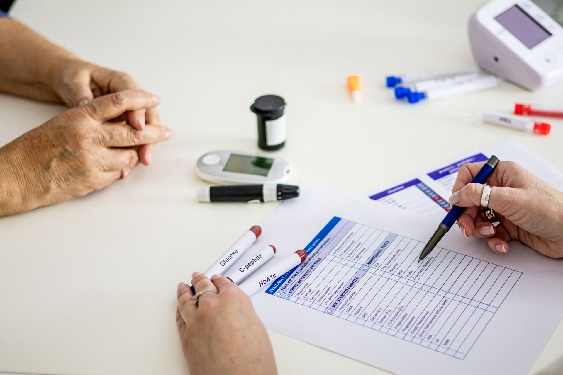 Close-up of hands of an unrecognizable old woman and doctor in doctor's office. Senior woman patient having geriatric doctor examining, consulting and diagnosing about hormone status, diabetes and thyroid hormones.